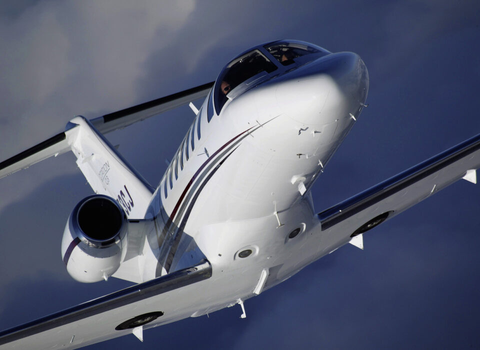 A light jet aircraft flying against a backdrop of blue sky and clouds.