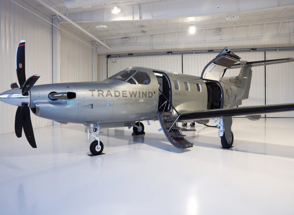A propeller aircraft labeled 'TRADEWIND' parked inside a hangar.