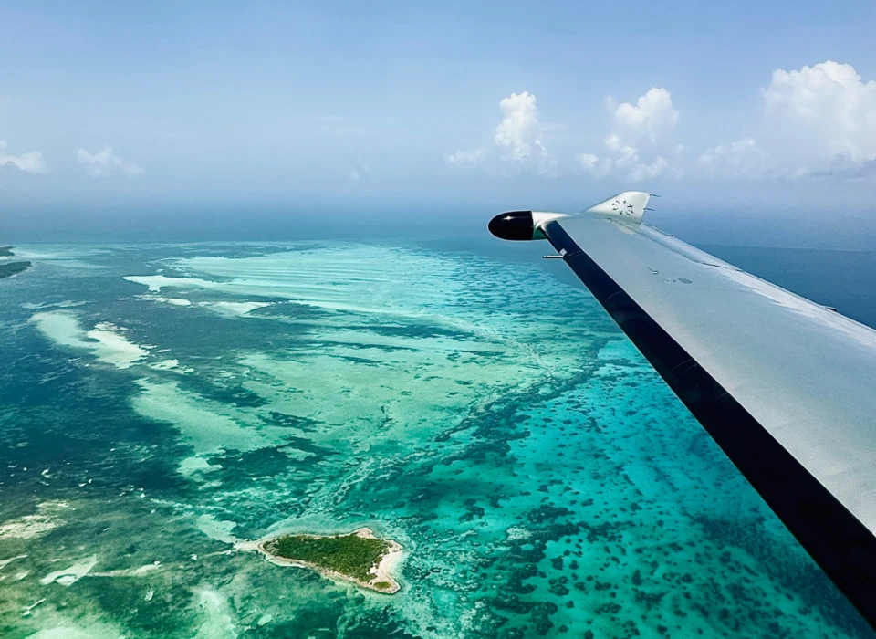 Aerial view from a plane wing, overlooking the blue waters of the Bahamas with islands scattered across the horizon.