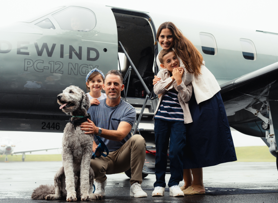 A family of four with a dog in front of a Tradewind Pilatus private plane to a resort that allows dogs