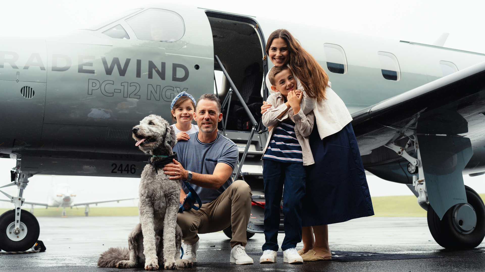 A family of four with a dog in front of a Tradewind Pilatus private plane to a resort that allows dogs