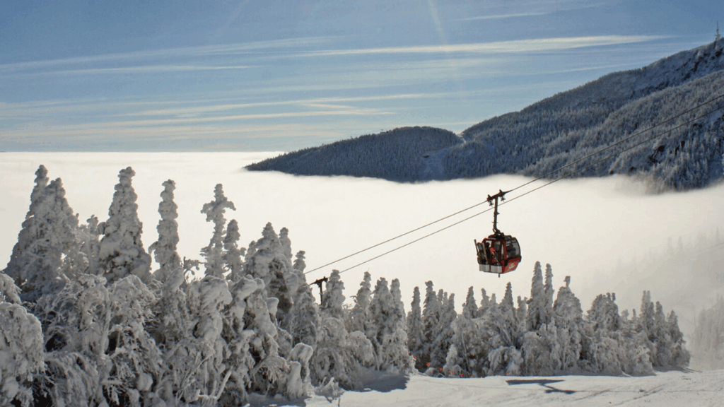 A red gondola at Stowe resort with cloud covered snowy peaks