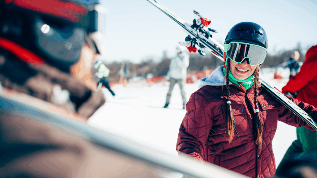 Female skier in a burgundy jacket with skis over her shoulder