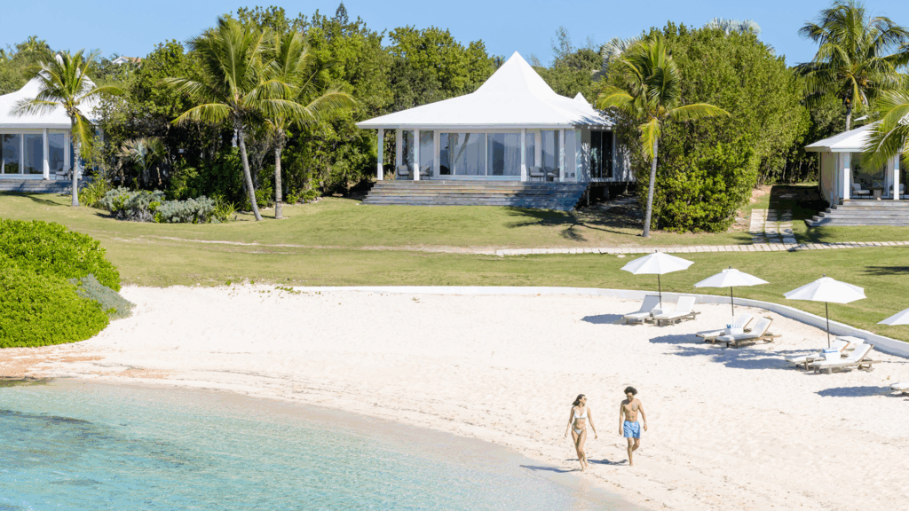 White beach cottages and a couple walking along sandy shores in the Bahamas
