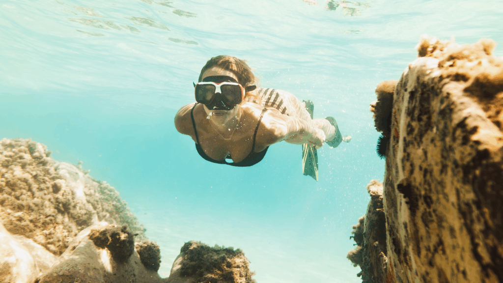 A woman with goggles on snorkeling through turquoise waters in Eleuthera.