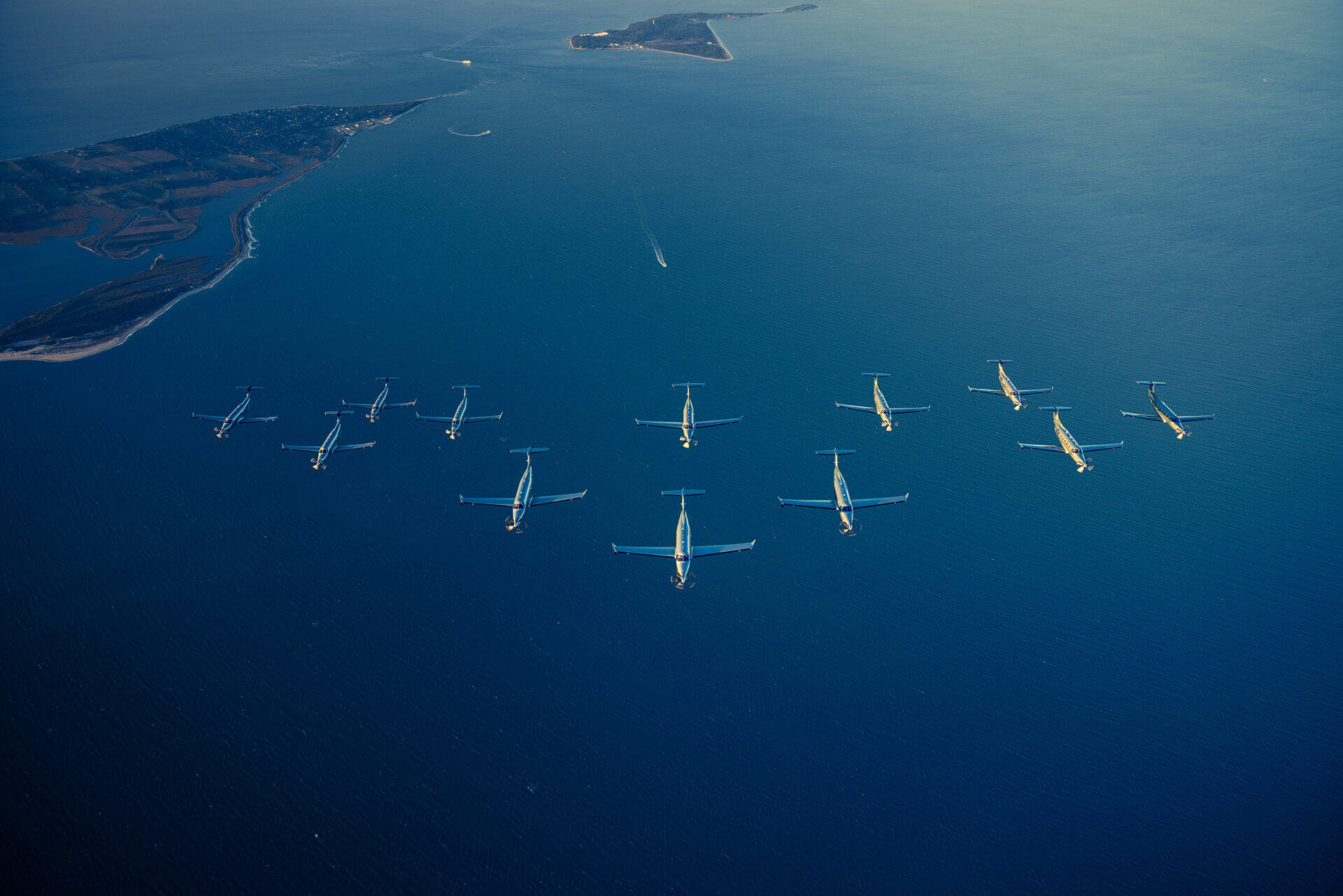 Aerial view of multiple Tradewind Aviation Pilatus PC-12 aircraft flying in formation over the blue waters.