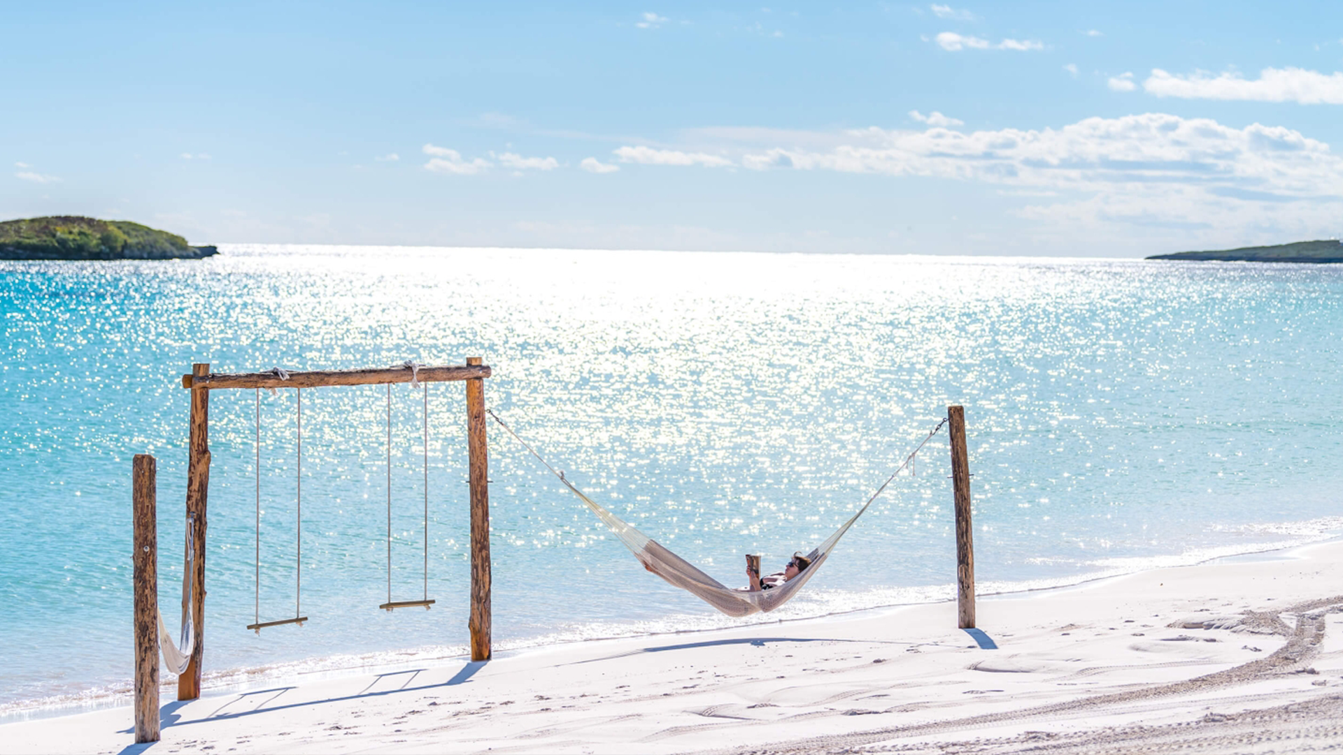 A woman laying in a beach hammock with turquoise waters behind.